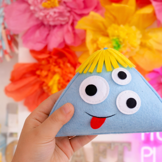 child hand holding a felted creation in front of paper flowers