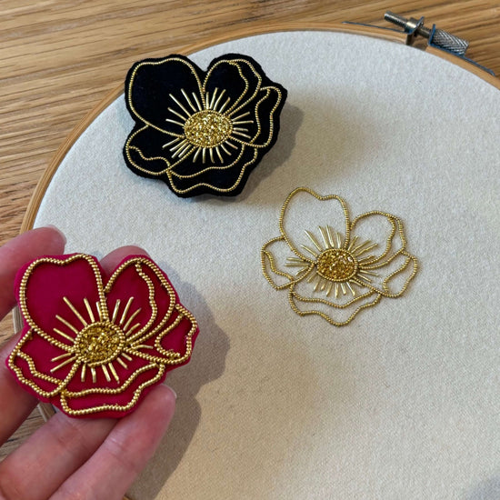 Embroidered flowers on a wooden hoop with a hand holding a red flower patch.
