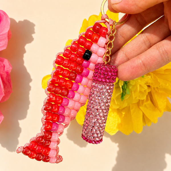 Hand holding a pink and red beaded seahorse keychain with a clear crystal charm against a yellow floral background.