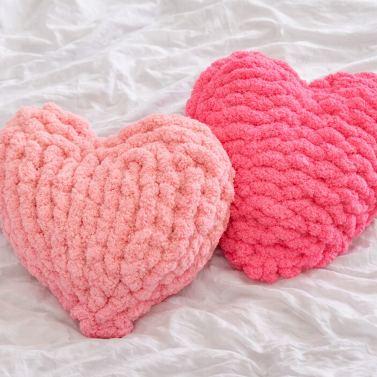 Two pink heart-shaped cushions on a white bed sheet