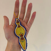 Hand holding a yellow 3D beaded and goldwork decorative item with blue and red details against a plain background