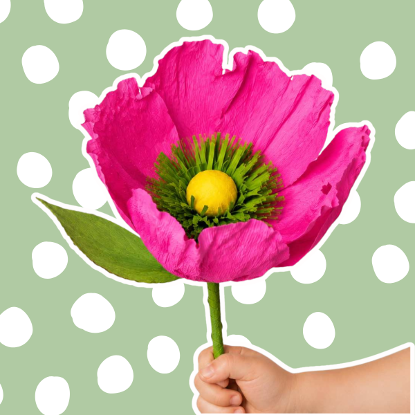 Hand holding a giant pink flower against a green background with white polka dots