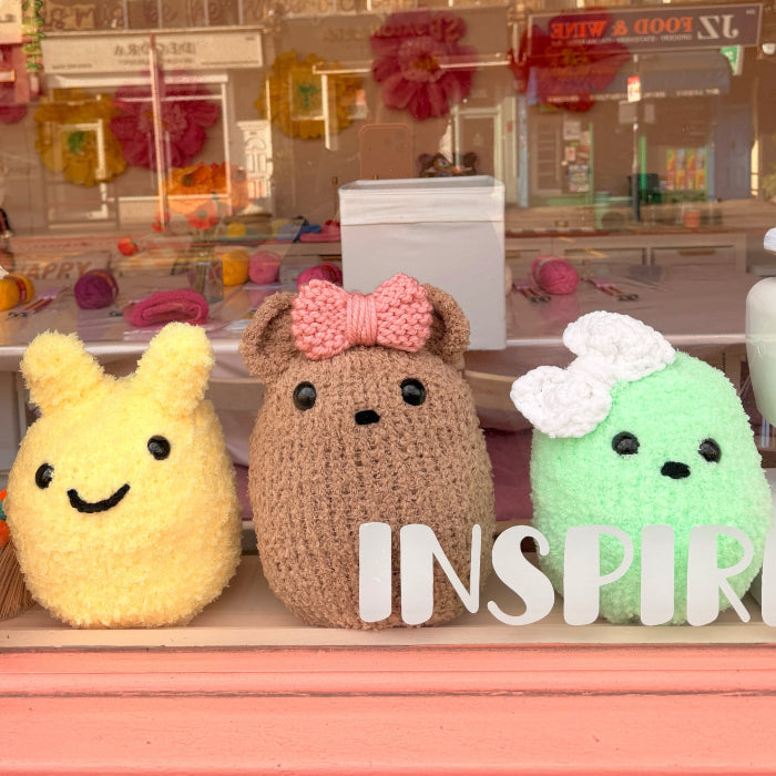 Three colorful plushie toys hand knitted with a 'INSPIRE' sign in a shop window