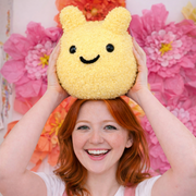 Person holding a yellow plushie toy with a smiley face against a paper floral background