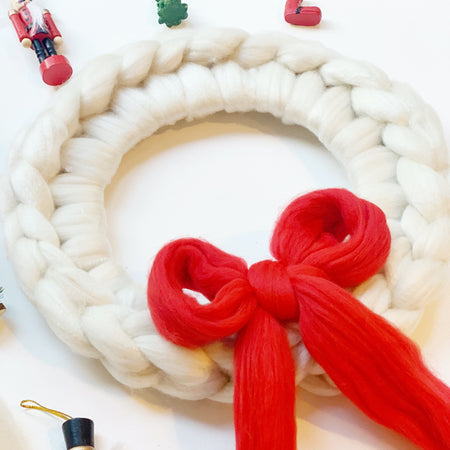 A completed arm knit Christmas wreath with a red bow on a white background, surrounded by festive decorations.